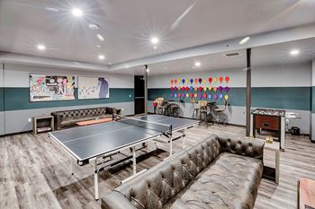 A ping pong table is in the middle of a room with a couch and a bar.